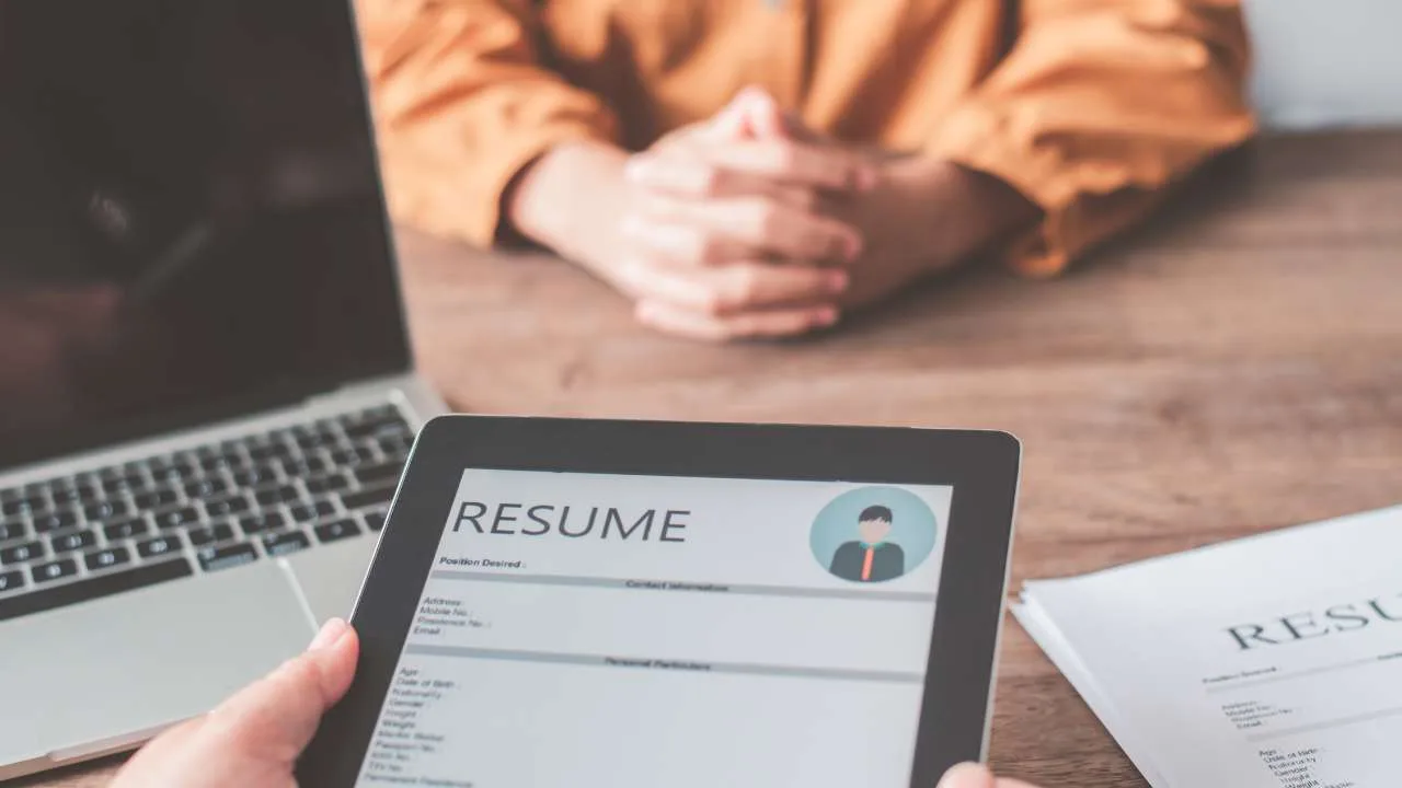 Currículum en una tablet mostrado durante una entrevista de trabajo, con una persona sentada al fondo.