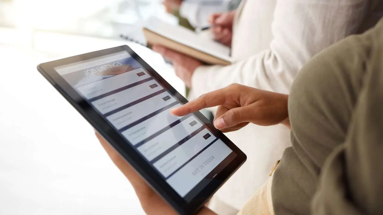 Persona interactuando con una tablet que muestra listados de empleo en una pantalla.
