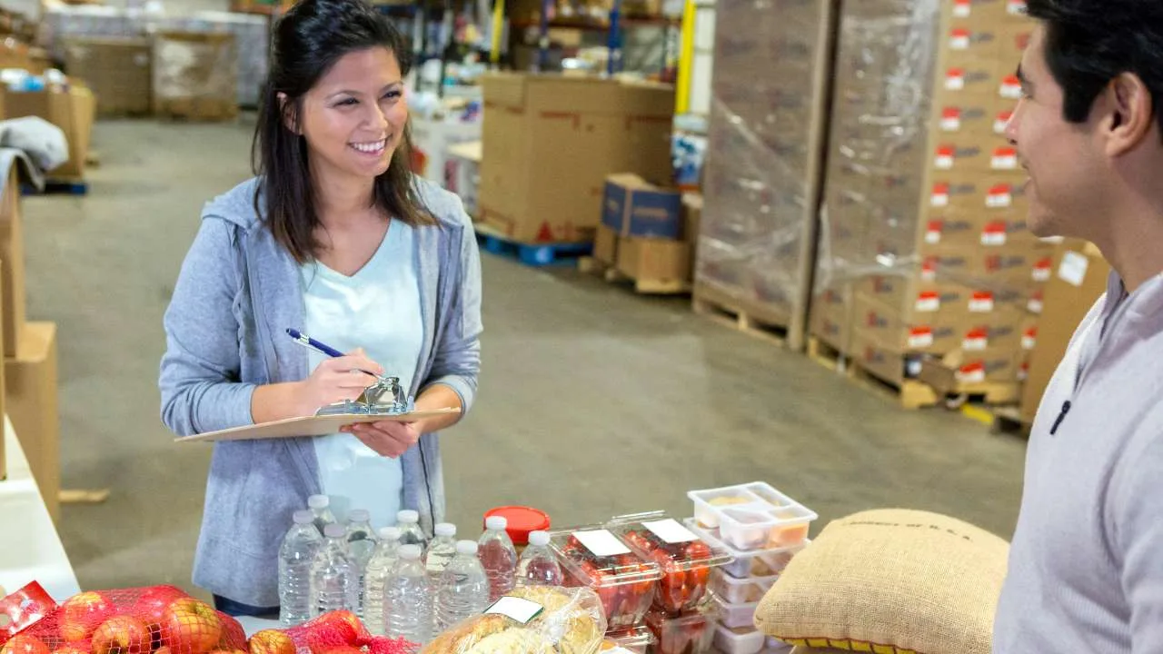 Mujer sonriendo mientras sostiene un clip con una lista en un banco de comida.