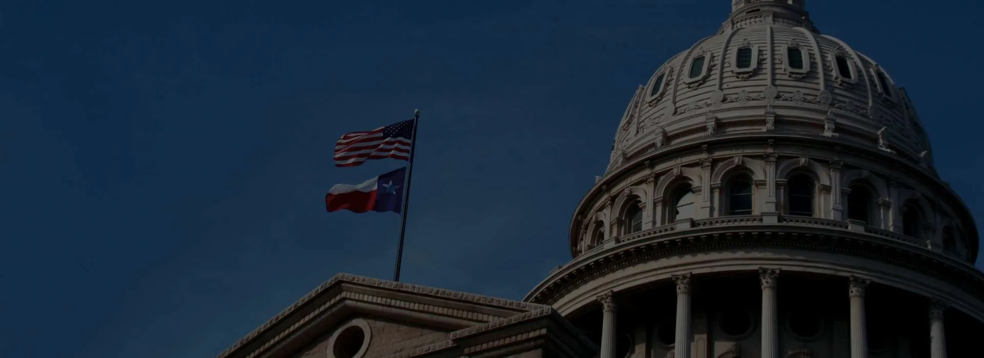 Cúpula del Capitolio de Texas con la bandera de Estados Unidos y la bandera de Texas ondeando.