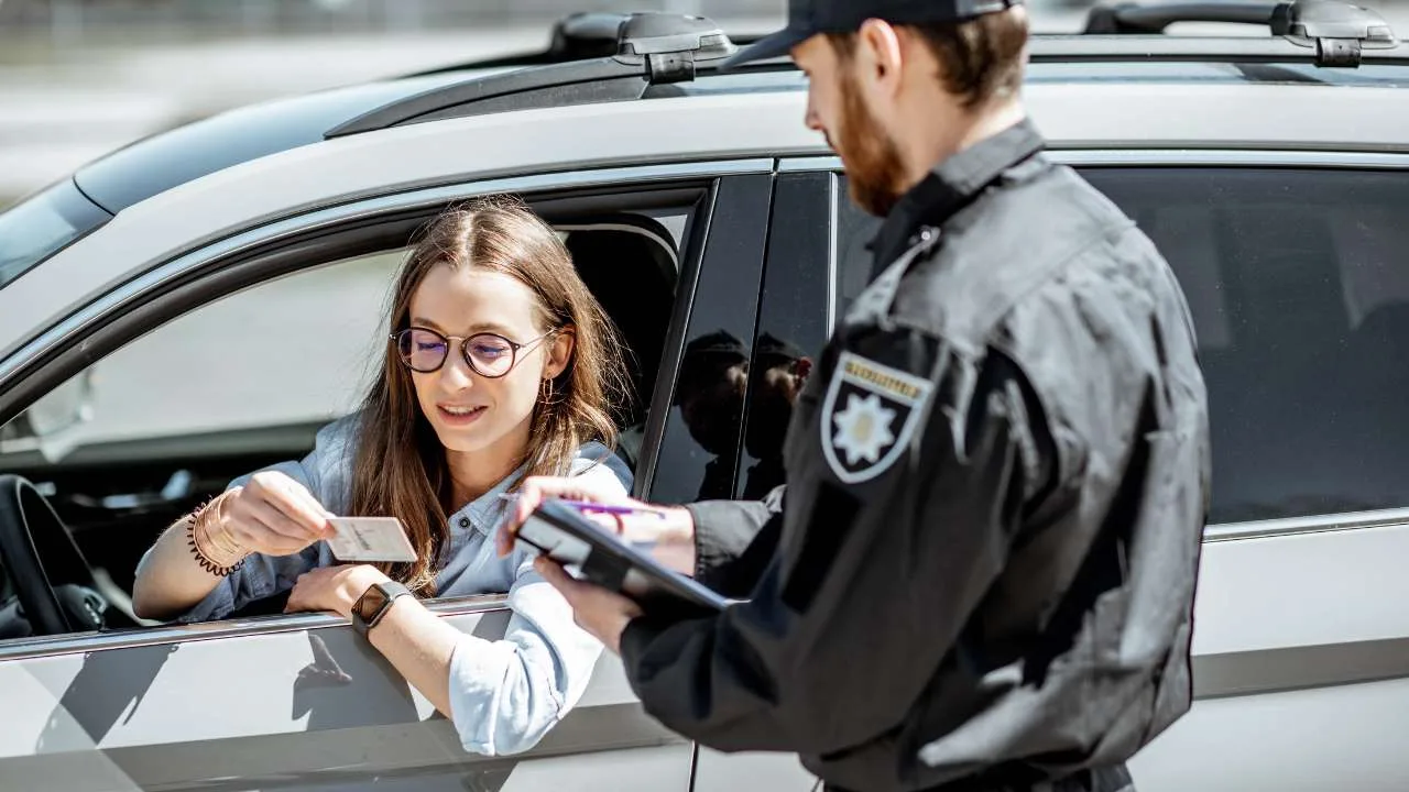 Una mujer mostrando su identificación a un oficial de policía mientras está en un vehículo.