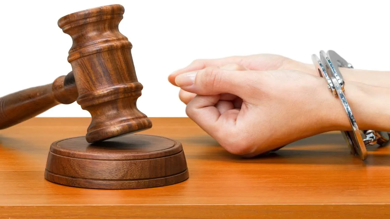 Martillo de juez de madera junto a una mano con esposas sobre una mesa.