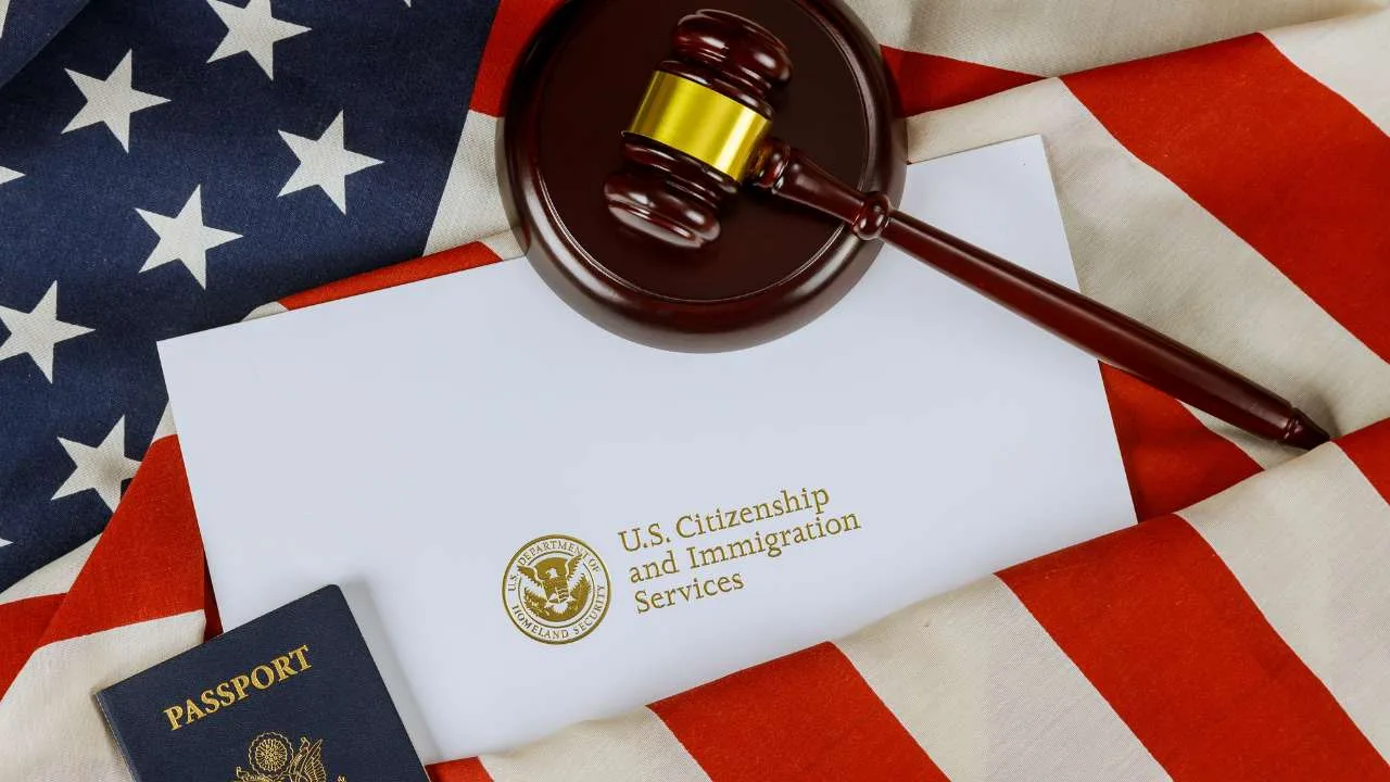 Sobre de U.S. Citizenship and Immigration Services con un pasaporte y un martillo sobre una bandera estadounidense.