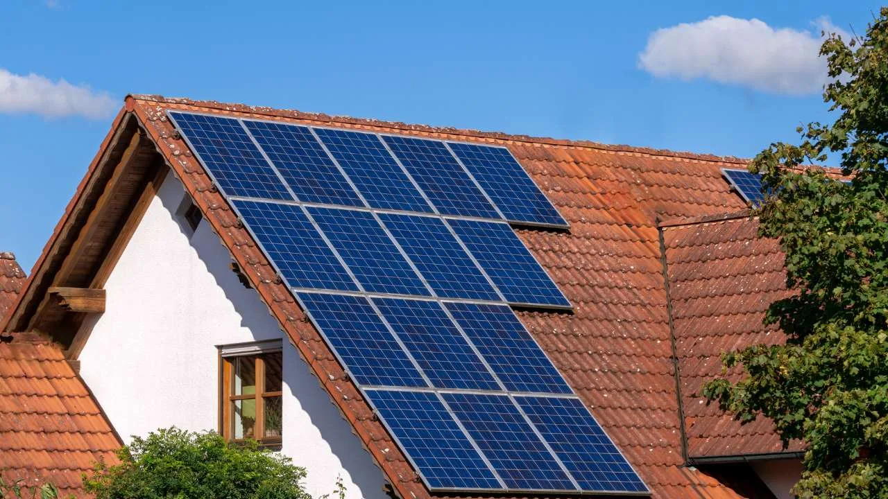 Paneles solares instalados en el techo de una casa con tejas rojas y cielo azul.