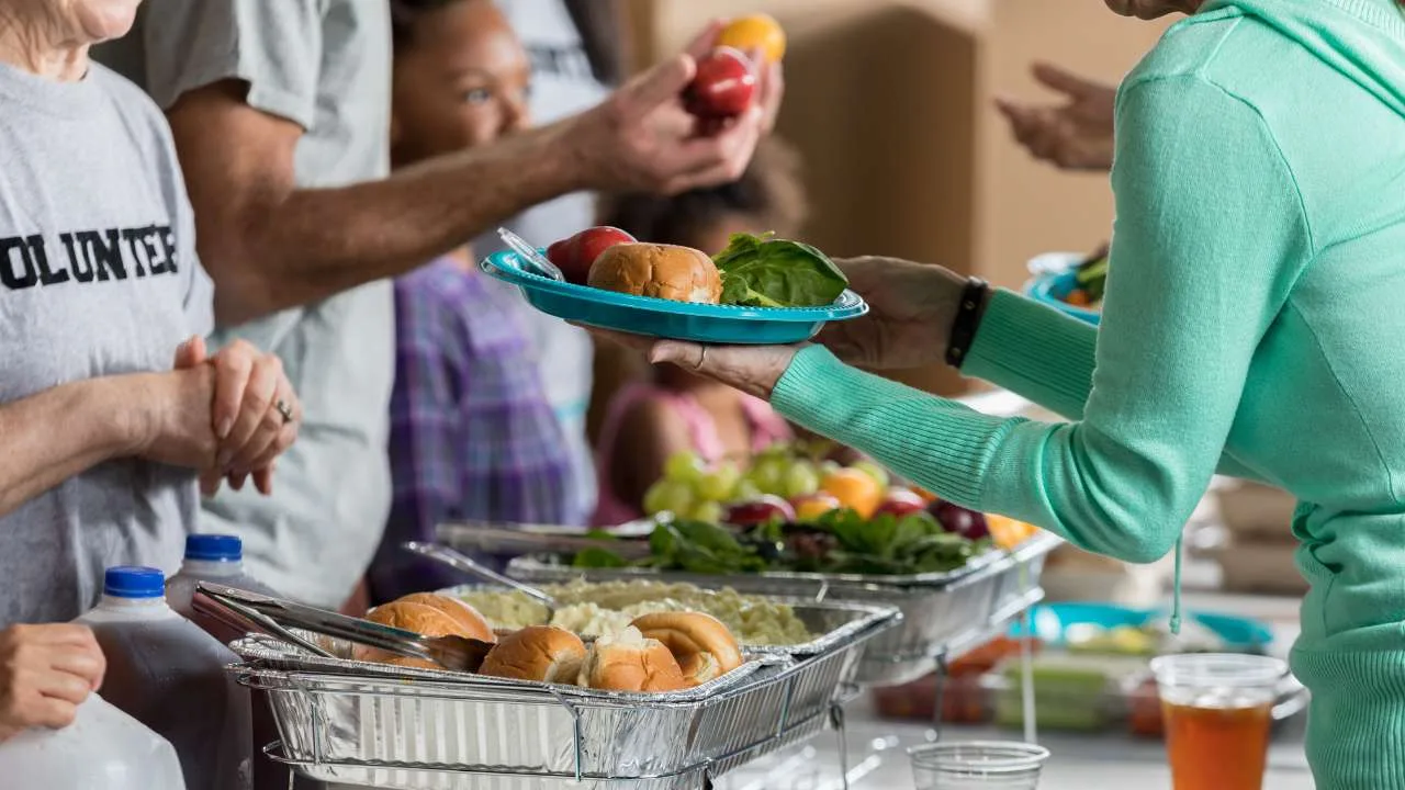 Personas sirviendo y recibiendo platos de comida en un evento de distribución de alimentos.