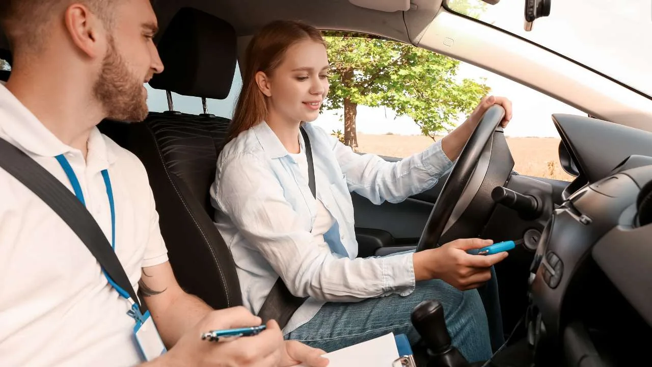 Una mujer al volante de un automóvil mientras un instructor toma notas en una hoja de papel.