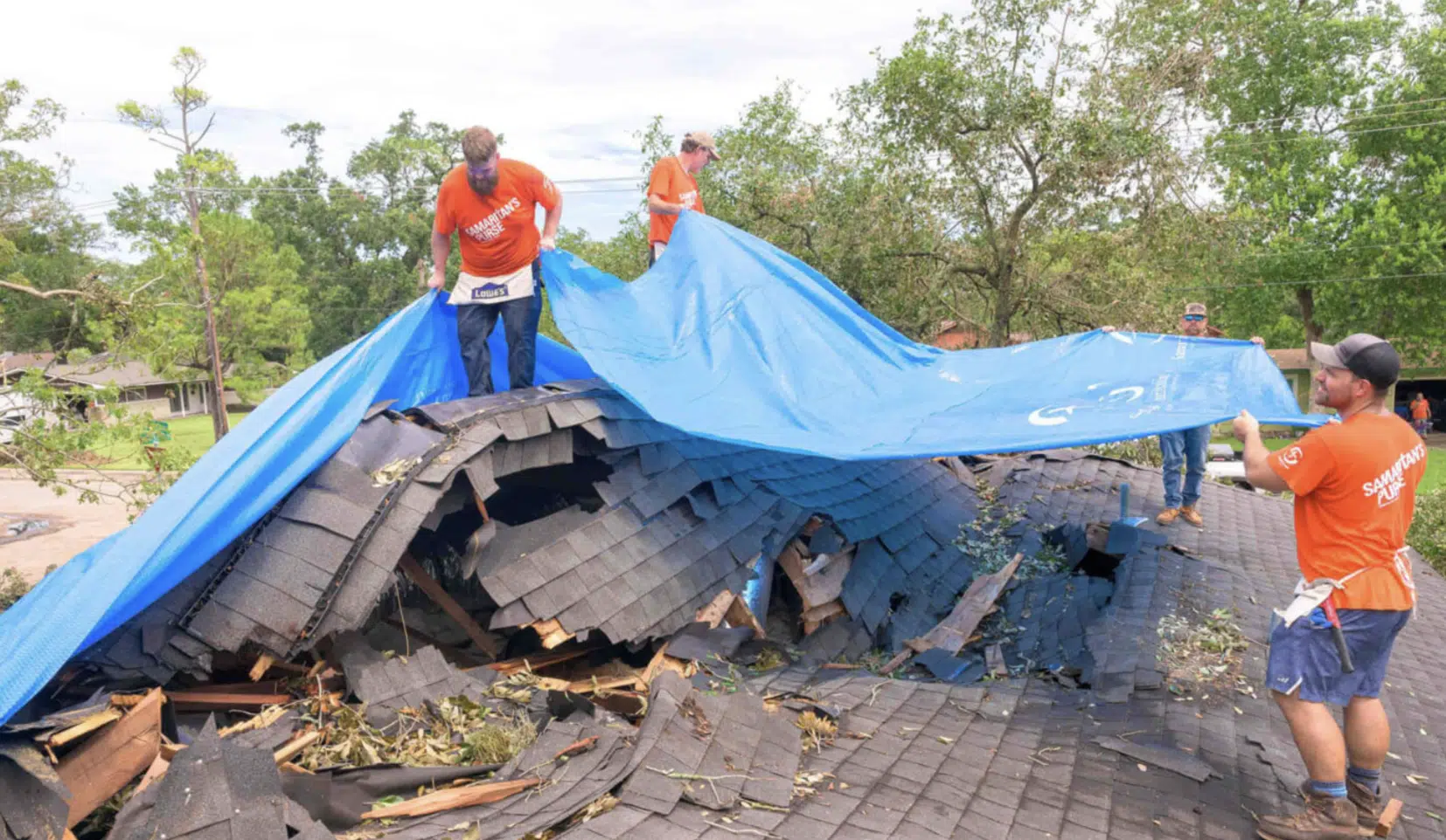 Hombres trabajando en un techo dañado, cubriendo con una lona azul después de una tormenta.