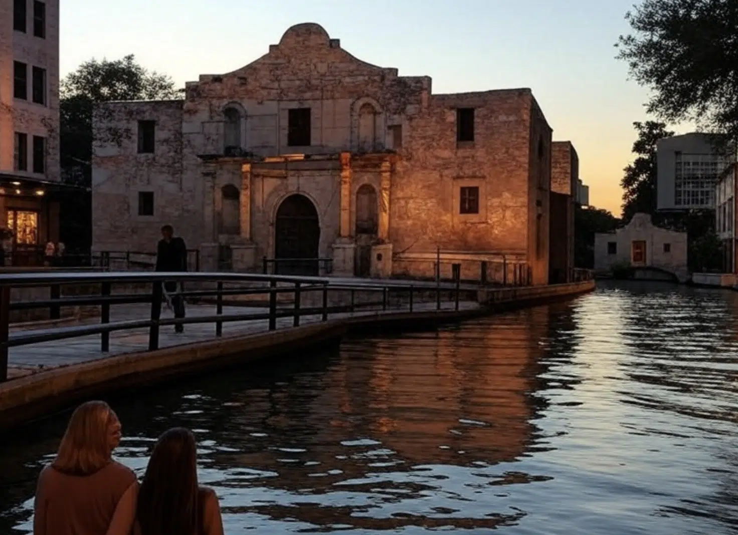 Edificio de piedra iluminado al atardecer junto a un canal con personas en primer plano.