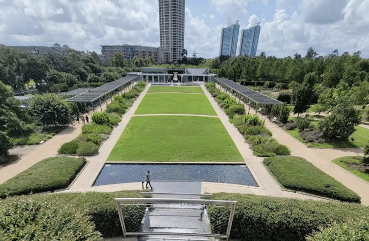Vista aérea de un jardín paisajístico con césped verde y senderos en un entorno urbano.