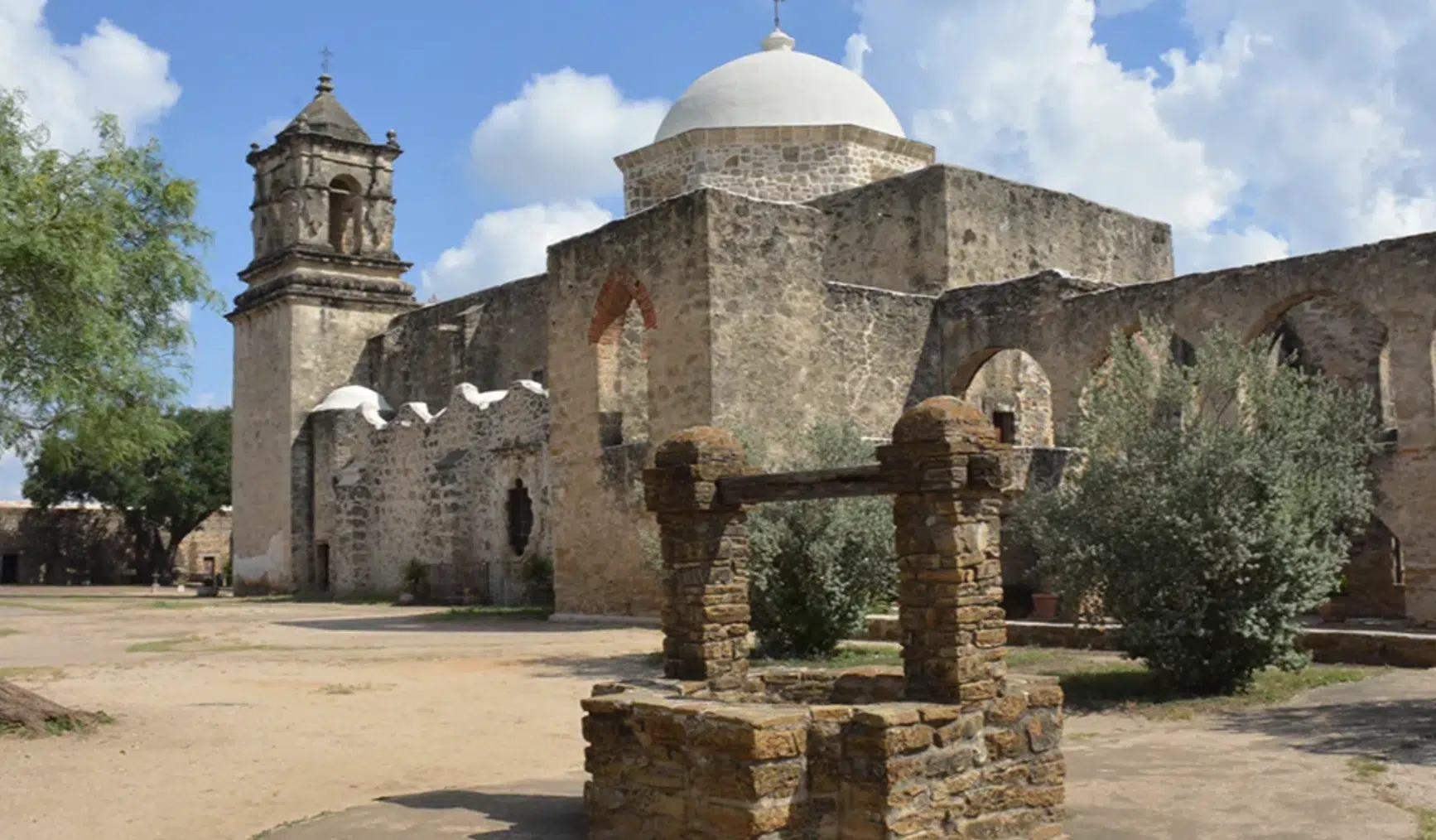 Edificio de misión histórica con campanario y pozo de piedra en el primer plano.
