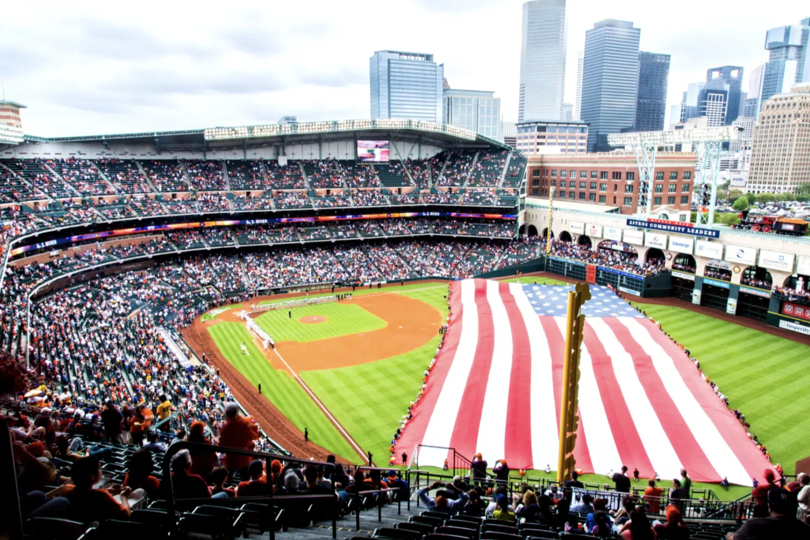 Vista panorámica de un estadio de béisbol con una gran bandera estadounidense en el campo.
