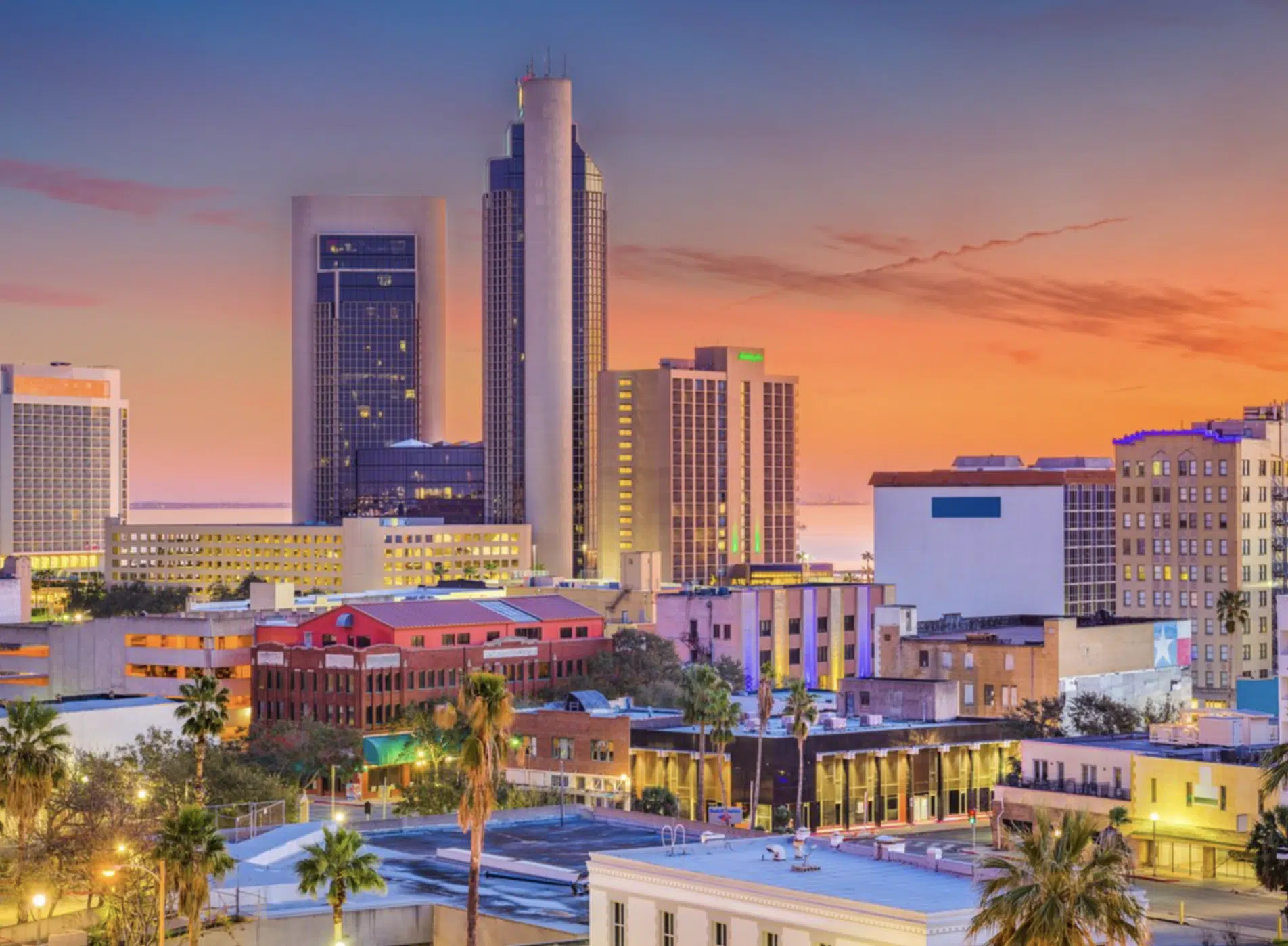 Vista de edificios y skyline de Corpus Christi al atardecer con colores cálidos en el cielo.